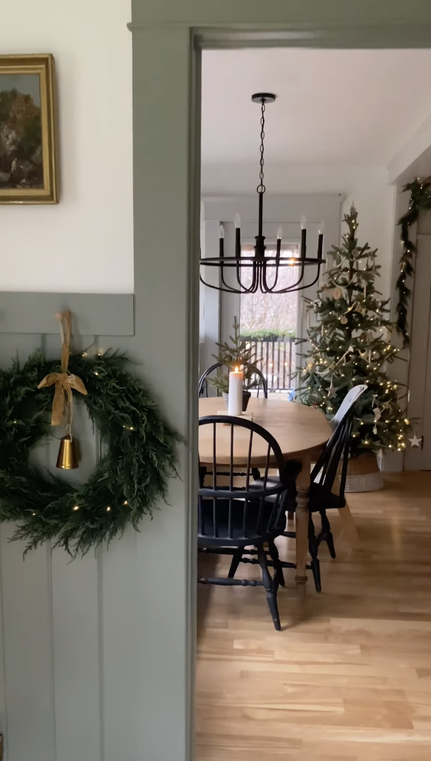 modern farmhouse dining room with minimalist Christmas tree, greenery wreath, and black chandelier for cozy holiday home decor
