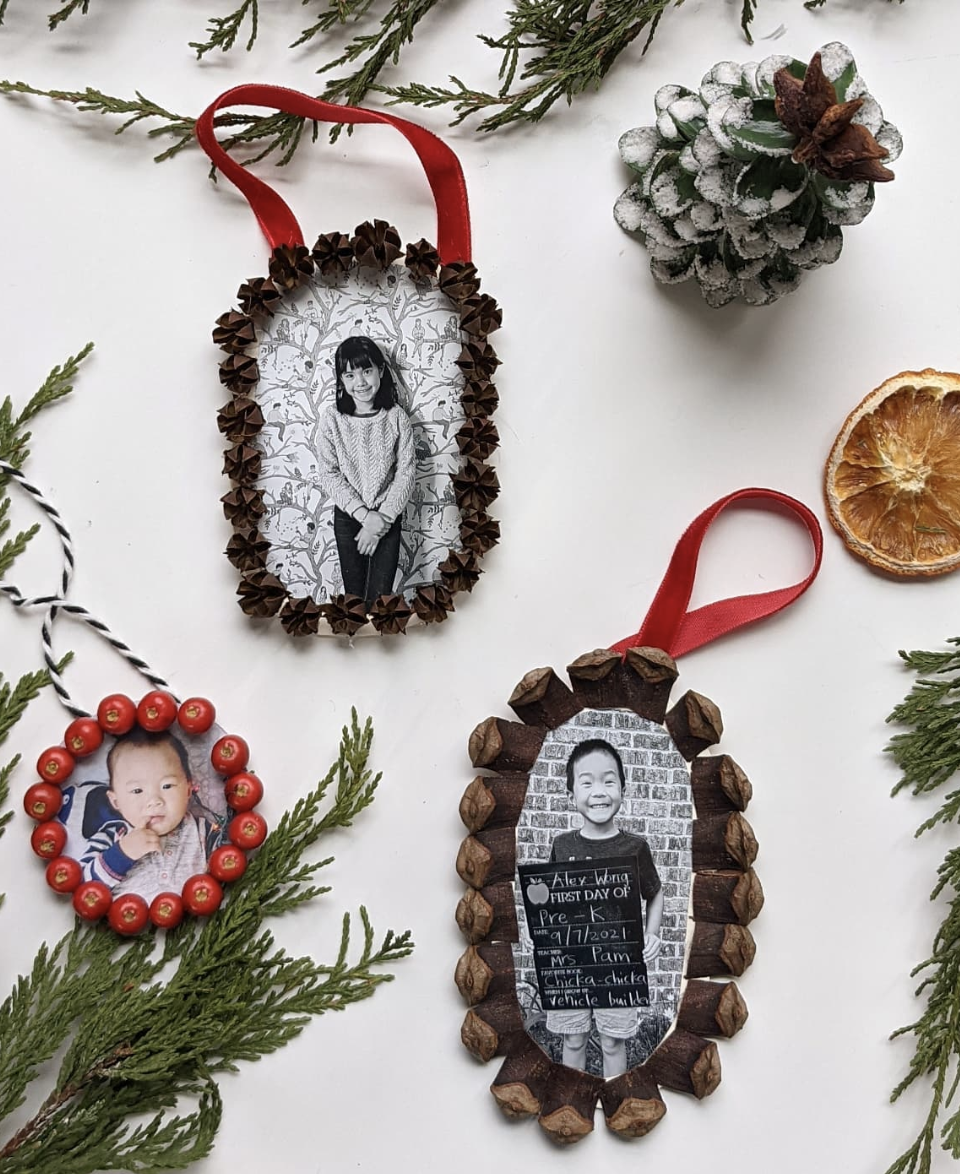 DIY nature-inspired photo ornaments decorated with pinecones, dried pods, and red berries framing black and white children's photos on a white background with holiday greenery