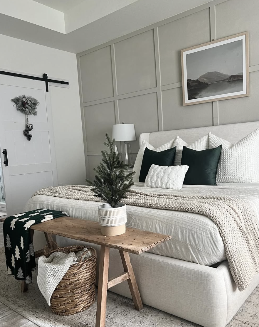 neutral farmhouse christmas bedroom with green pillows, cozy knit blankets, and small christmas tree decor