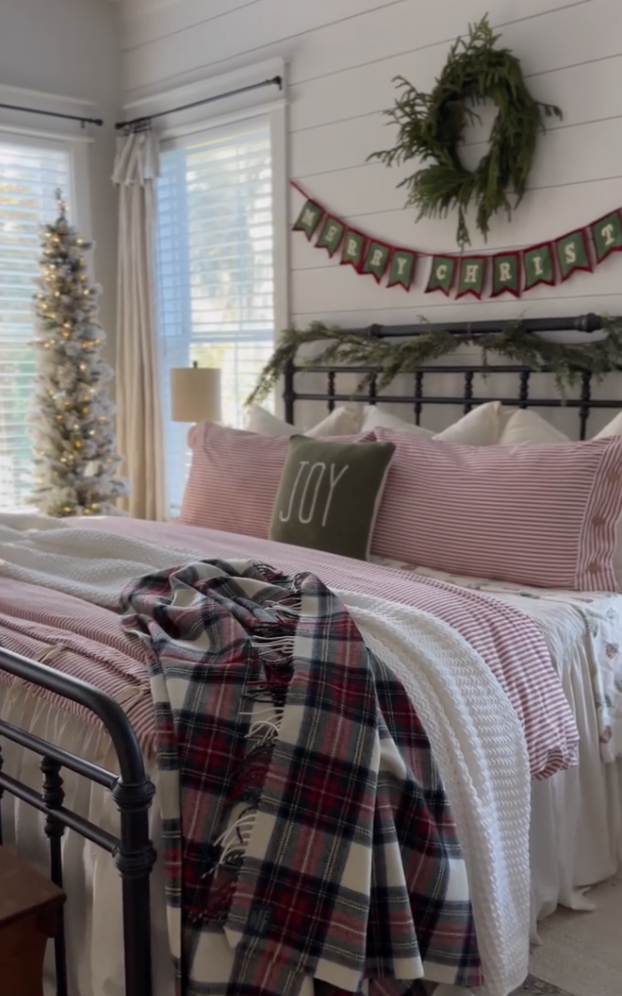 red and white farmhouse christmas bedroom with striped bedding, plaid blanket, and merry christmas banner over bed