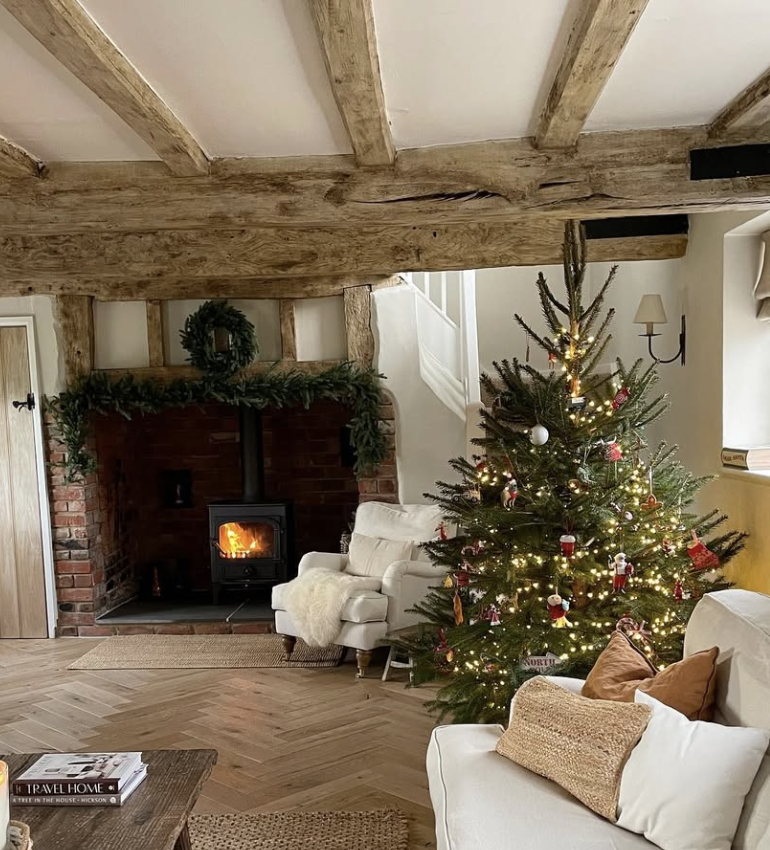 rustic farmhouse Christmas tree with glowing lights beside brick fireplace and wood beams in cozy country living room