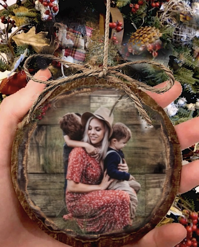 Rustic DIY wood slice photo ornament with a family picture sealed onto a wood round, finished with jute twine and bow, held in hand before a Christmas tree