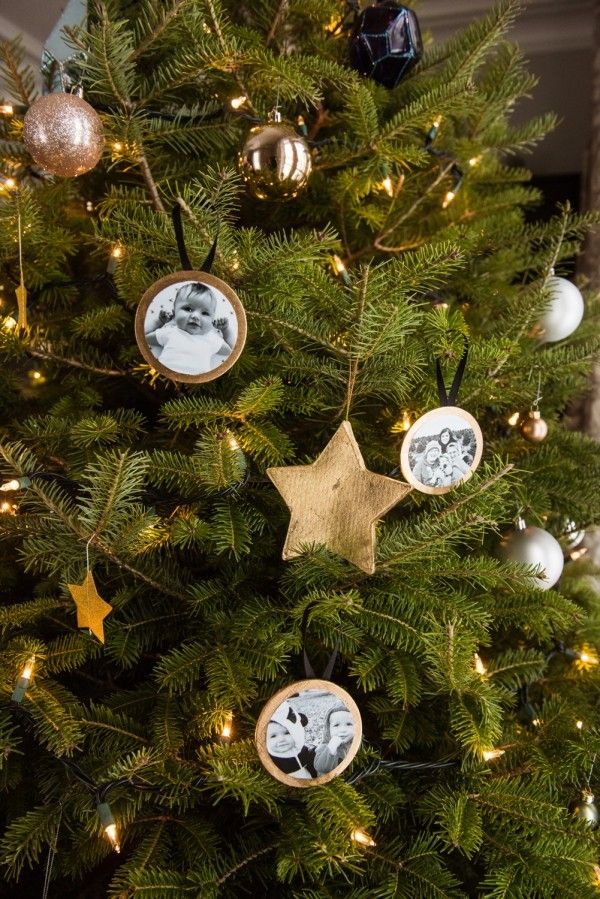 DIY rustic wood slice photo ornaments with black-and-white family photos hanging on a Christmas tree with gold stars and twinkle lights