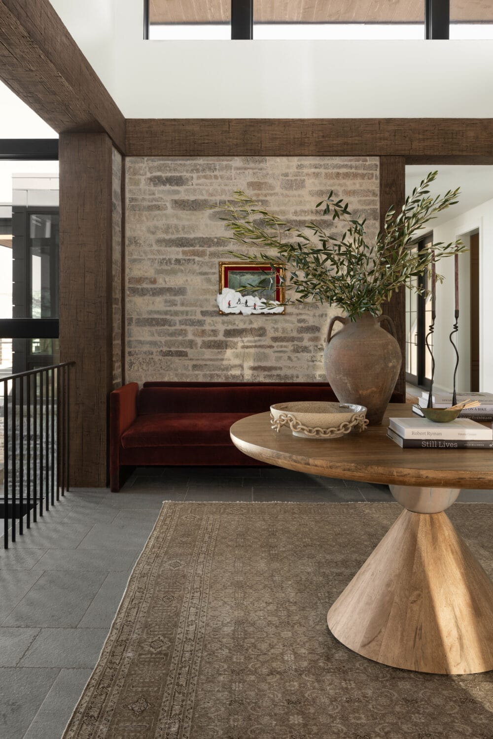 Studio McGee entryway with brick accent wall, round wood table, earthy vase with greenery, and burgundy velvet bench for a warm, textured design.