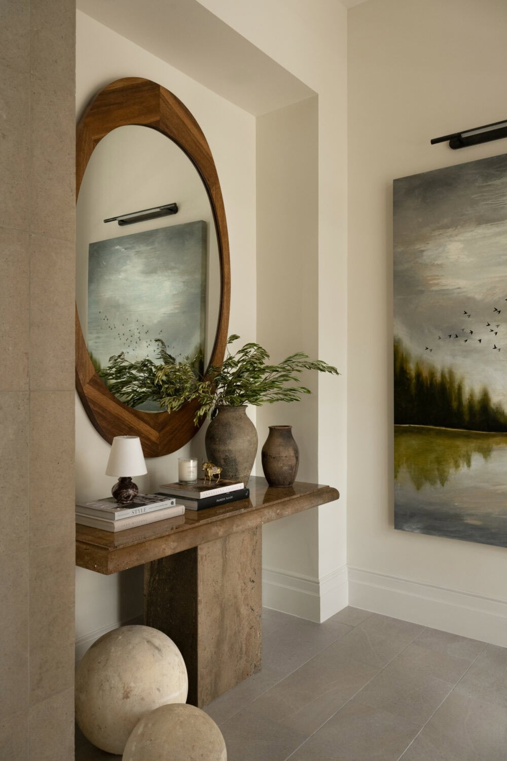 Studio McGee organic modern entryway with stone console, wood mirror, pottery vases, greenery, and landscape art in earthy neutral tones.