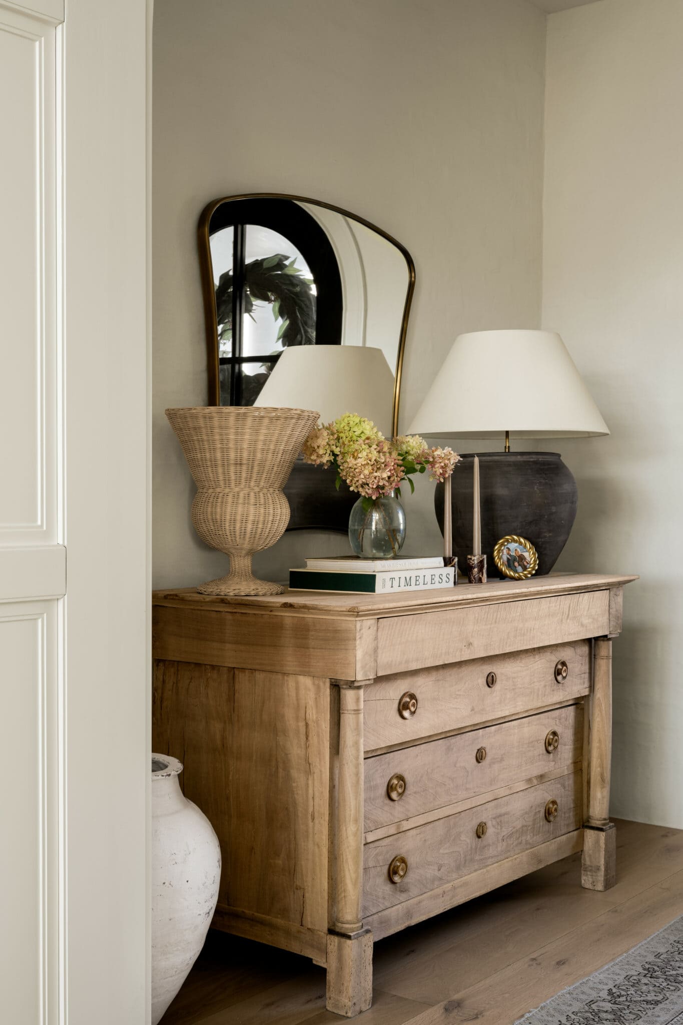 Studio McGee entryway with vintage wood dresser, arched mirror, table lamps, and floral arrangement creating a warm, timeless foyer display.