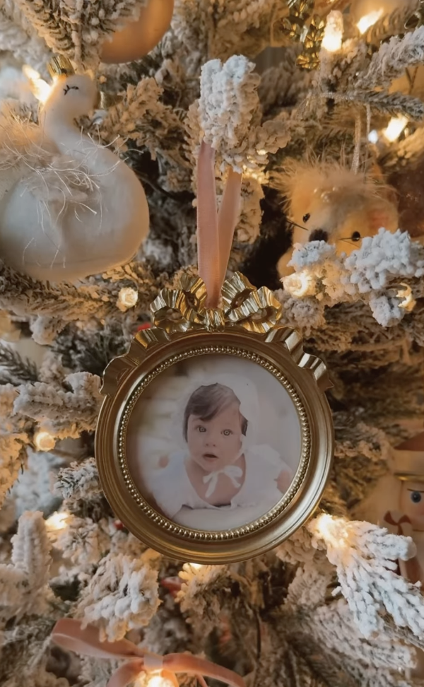 Vintage gold frame photo ornament with a baby picture hanging on a flocked Christmas tree with velvet ribbon and soft neutral decorations