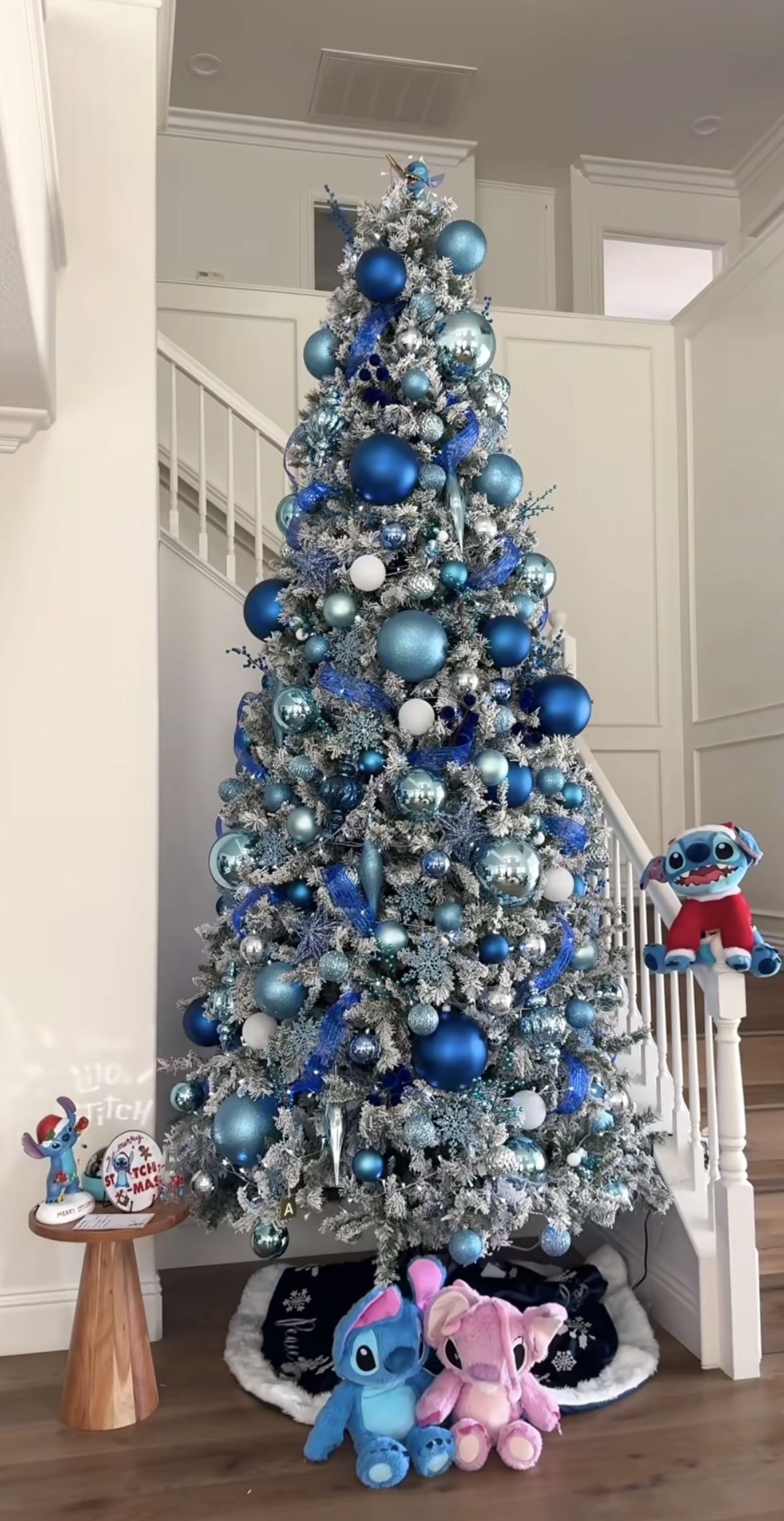 Flocked Christmas tree decorated in blue and silver ornaments with Stitch plush toys, blue ribbon, and icy holiday accents for a Lilo & Stitch Christmas theme.
