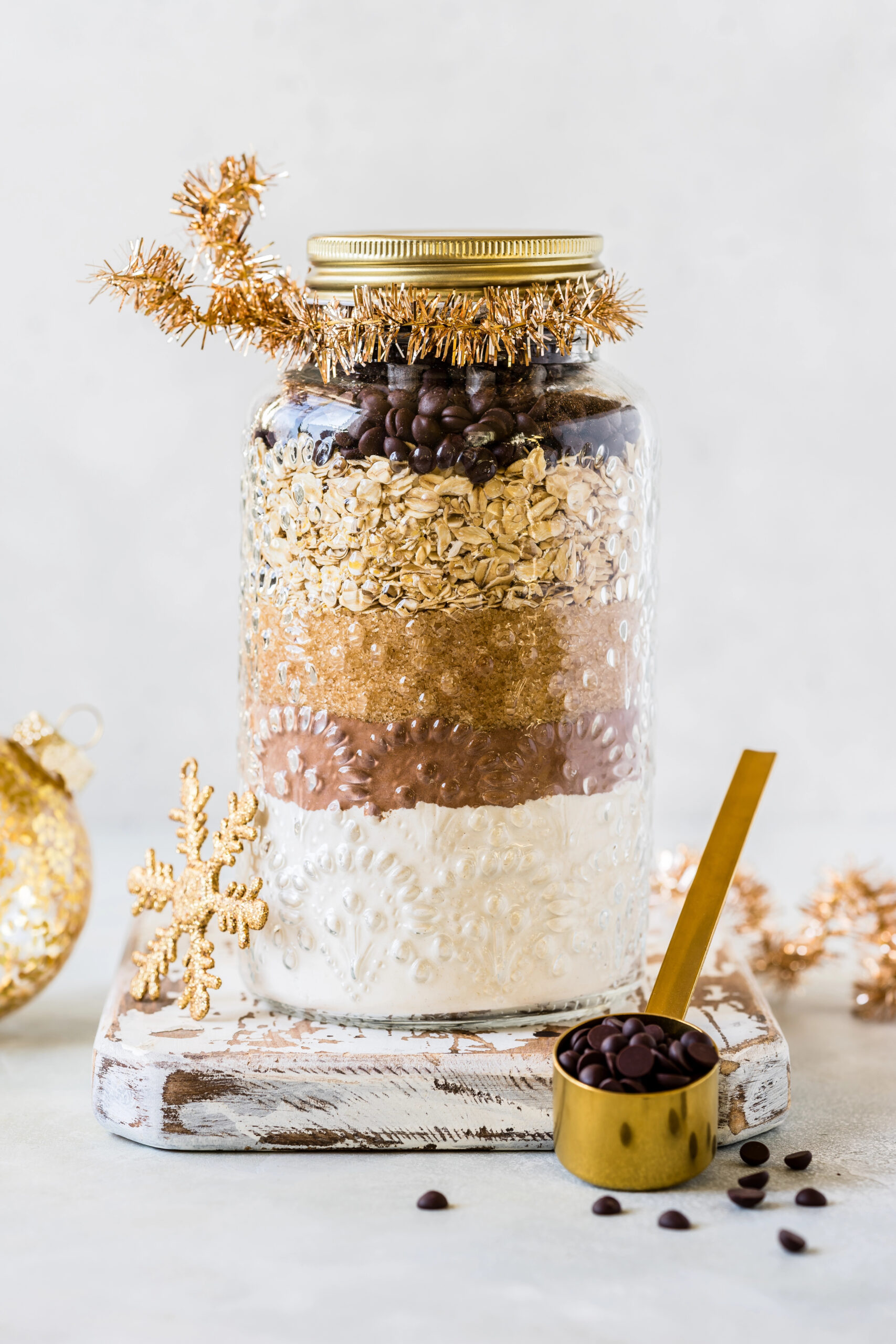 Layered cookie mix in a glass jar decorated with gold tinsel and holiday ornaments - an easy and thoughtful homemade homemaker gift idea for Christmas.