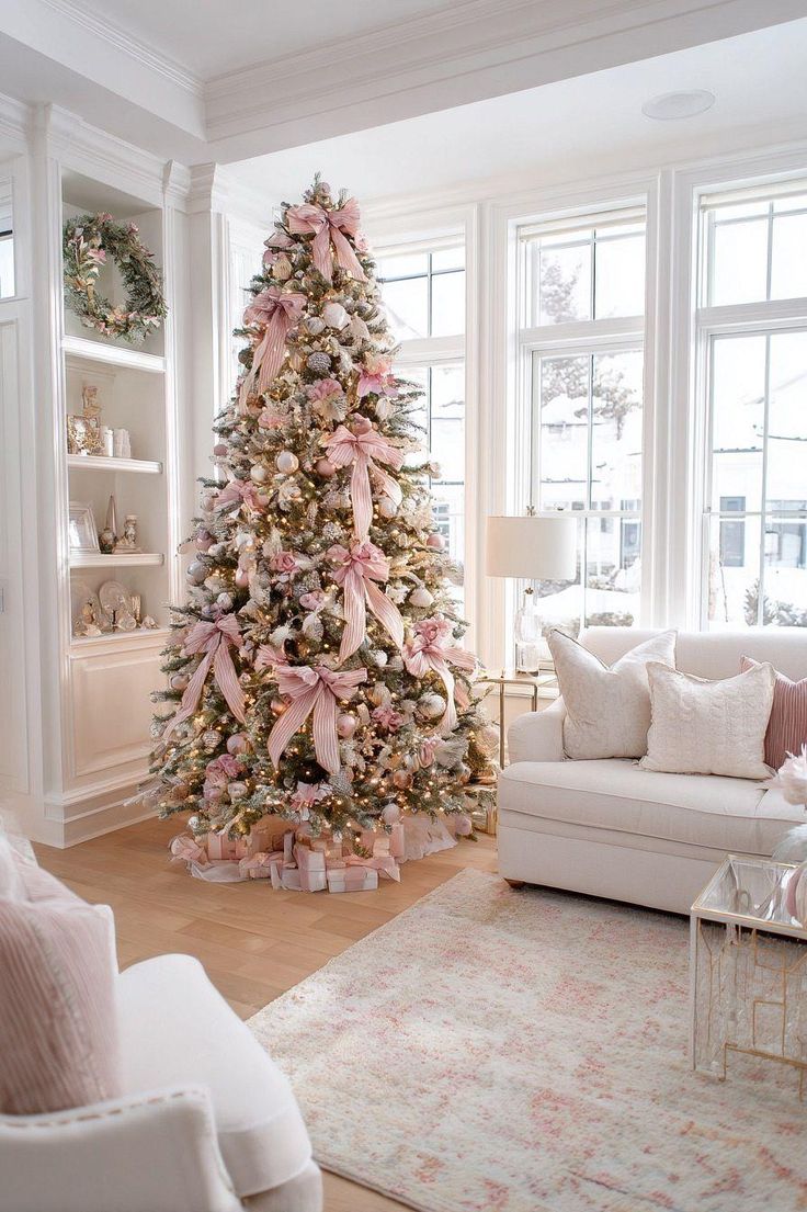 Tall Christmas tree decorated with pink ribbons, blush ornaments, and soft metallic accents in a bright, neutral living room.