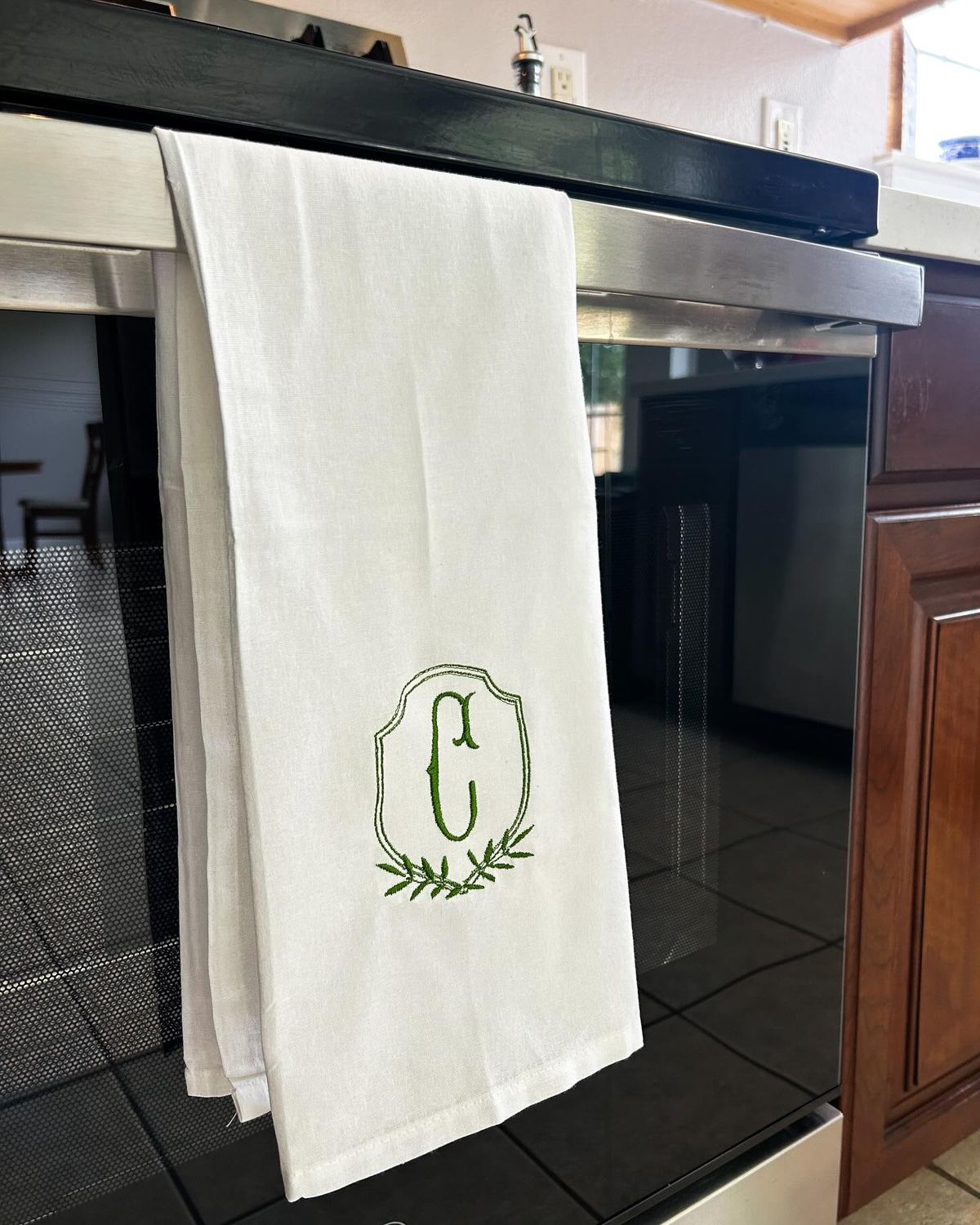 White linen tea towel with a green embroidered monogram hanging on an oven handle - an elegant and personal homemade homemaker gift idea for Christmas.