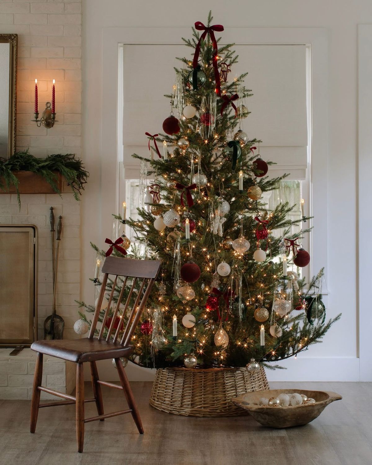 Elegant Ralph Lauren-inspired Christmas tree decorated with red velvet bows, gold and glass ornaments, and warm white lights, styled in a wicker basket base beside a wooden chair for a timeless, classic holiday look.
