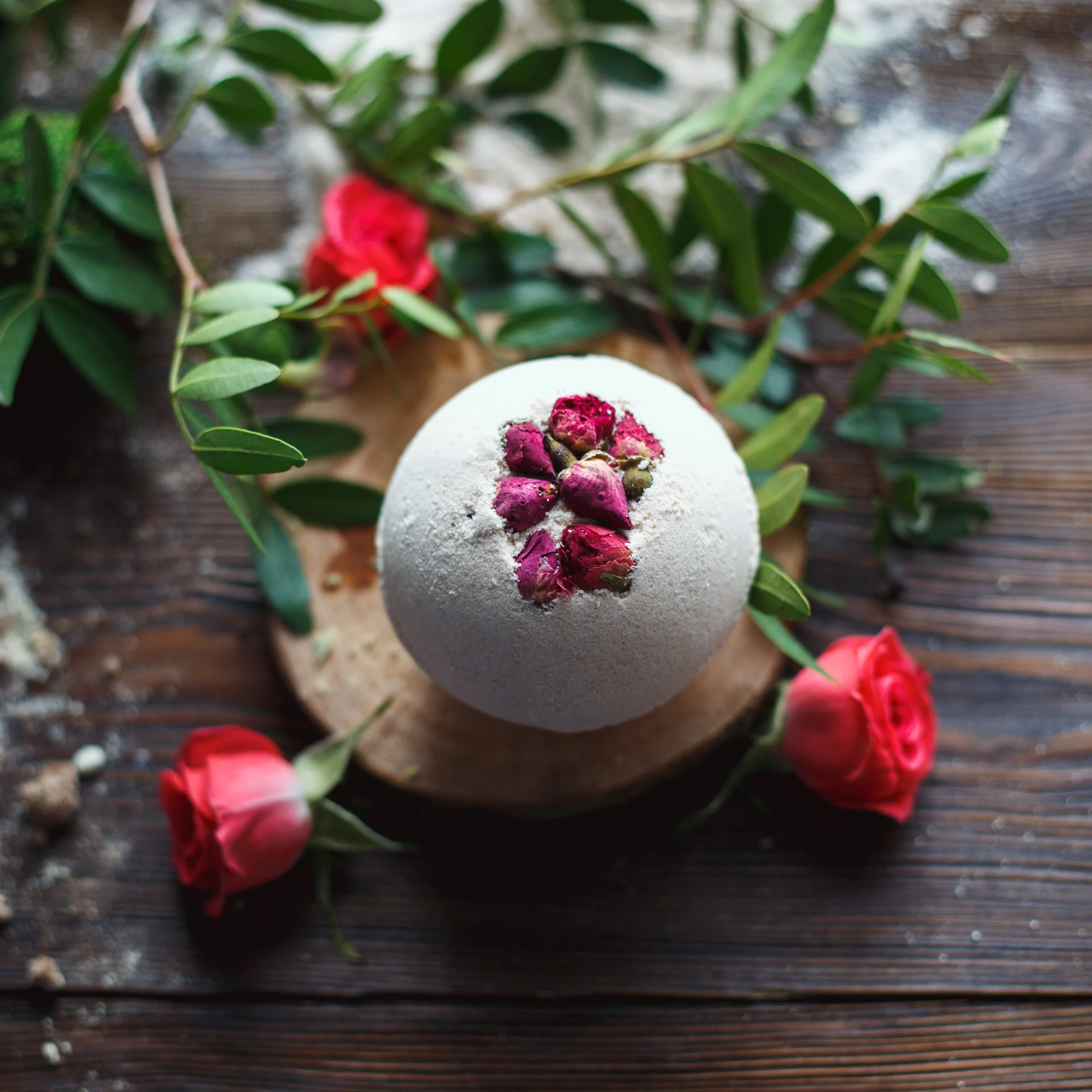 Homemade rose petal bath bomb surrounded by fresh roses and greenery on a rustic wooden table - a relaxing and elegant homemade homemaker gift idea for Christmas.