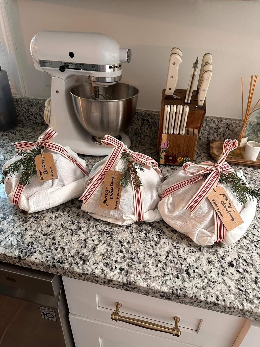 Wrapped sourdough starter kits tied with red striped ribbon and greenery on a kitchen counter - a cozy and thoughtful homemade homemaker gift idea for Christmas.