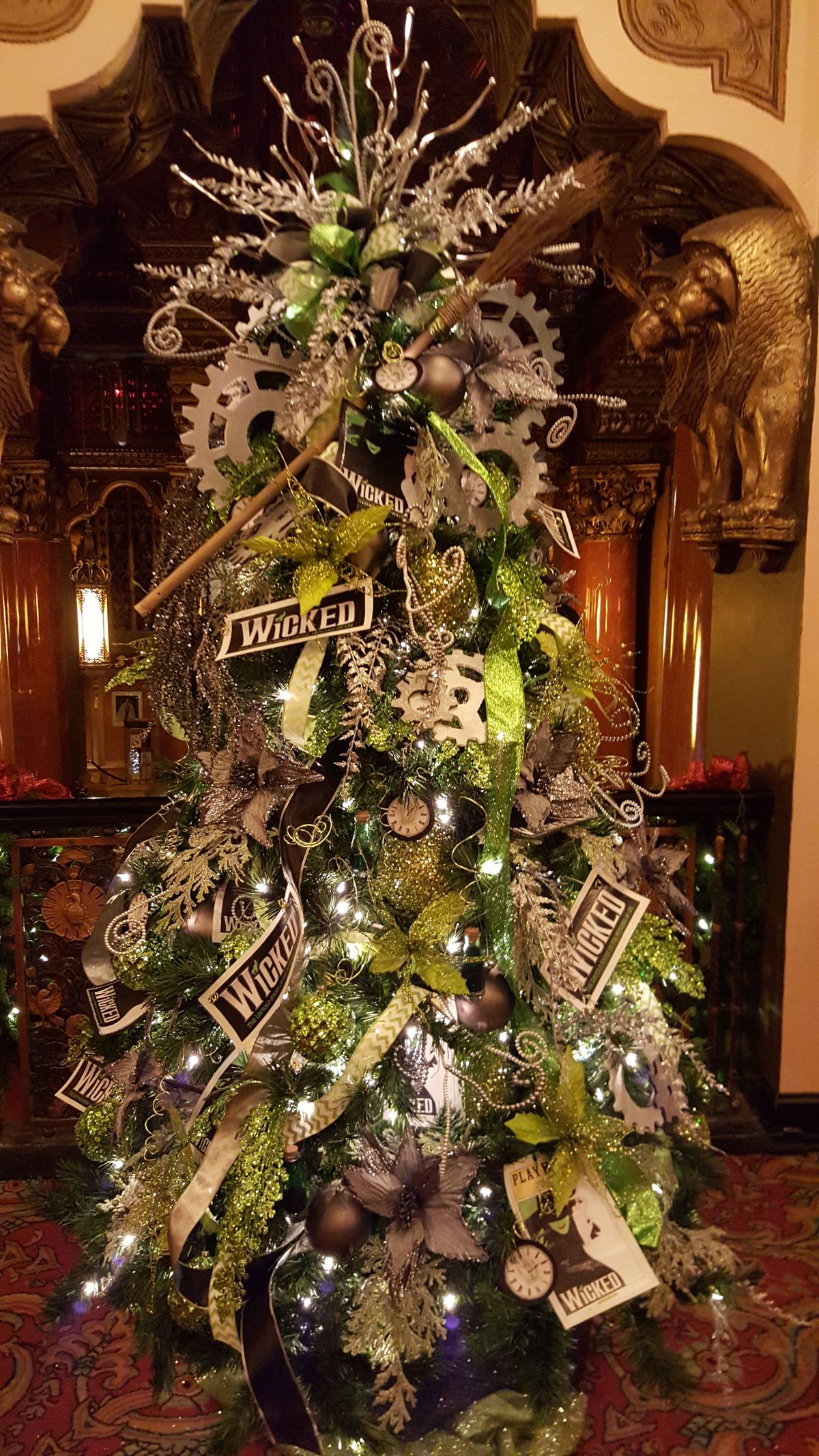 Wicked-themed Christmas tree decorated with green and silver ornaments, gears, glittering accents, and Wicked Broadway signage for dramatic holiday flair.
