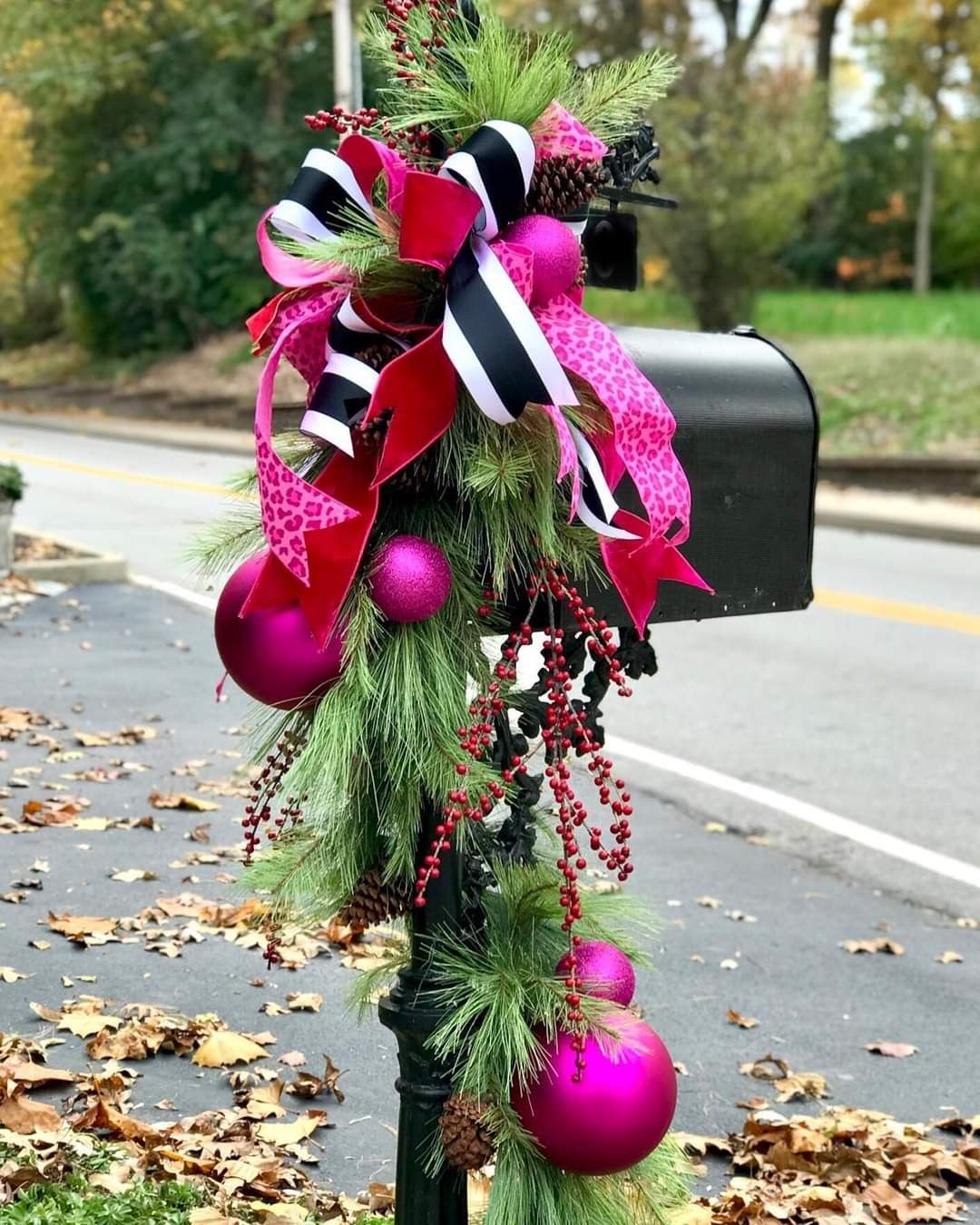Wicked-inspired Christmas mailbox garland with pine greenery, pink ornaments, black and white striped ribbon, and red berries.
