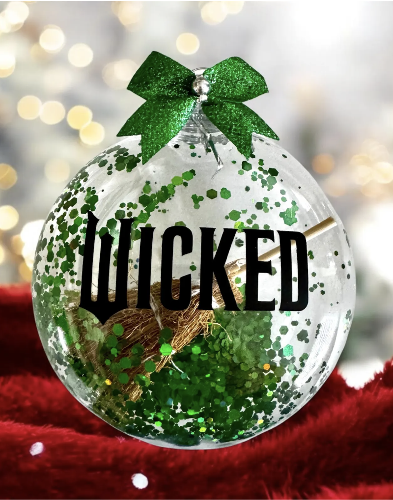 Clear Wicked Christmas ornament filled with green glitter and a tiny broom, topped with a sparkly green bow for a magical holiday touch.