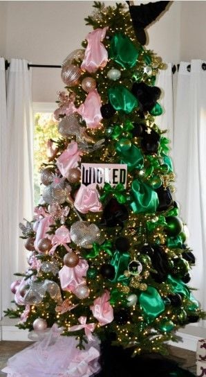 Wicked Christmas tree decorated with green, pink, and black ribbons, metallic ornaments, and a witch hat topper for a bold holiday statement.