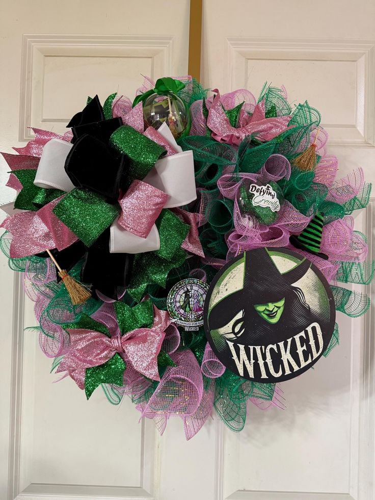 Wicked Christmas wreath made with pink and green mesh ribbon, glitter bows, and a Wicked witch logo centerpiece for a bold holiday look.