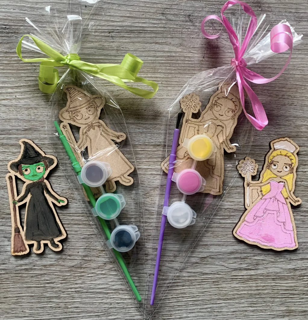 Wicked-themed wooden paint kits featuring Elphaba and Glinda characters with small paint pots and brushes tied in pink and green bows.