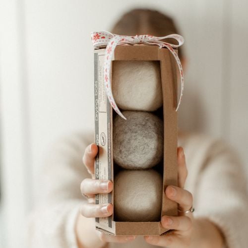 Hands holding a gift box of reusable wool dryer balls tied with festive ribbon - a sustainable and practical homemade homemaker gift idea for Christmas.