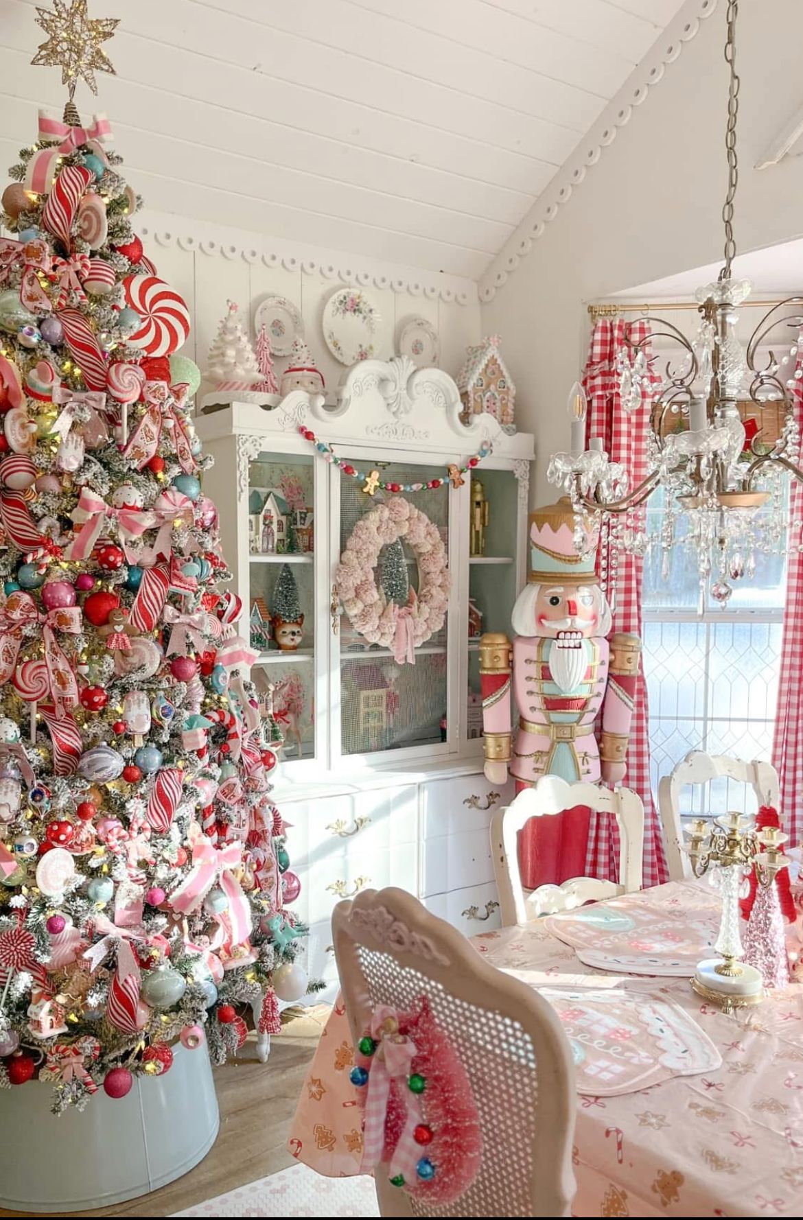 Candy-themed pink Christmas tree with oversized peppermint ornaments, pink ribbons, nutcracker decor, and festive holiday accents in a vintage-style dining room.