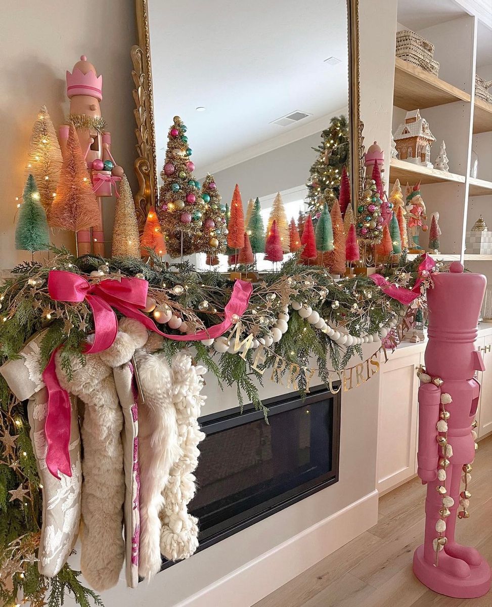 Festive Christmas mantel decorated with colorful bottle-brush trees, pink nutcrackers, garlands, and bright pink ribbon accents.