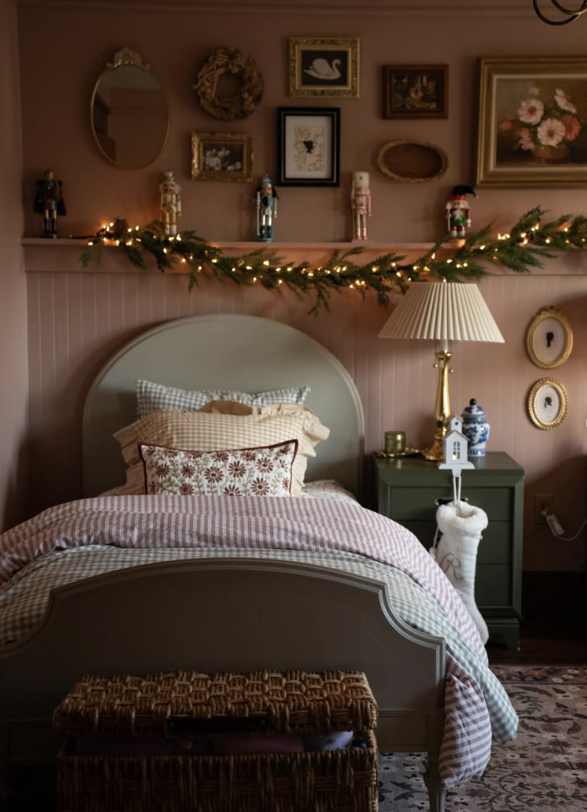 Cozy vintage-style bedroom decorated with warm gingham bedding, nutcracker figurines, gold frames, and a simple Christmas garland with soft lights.