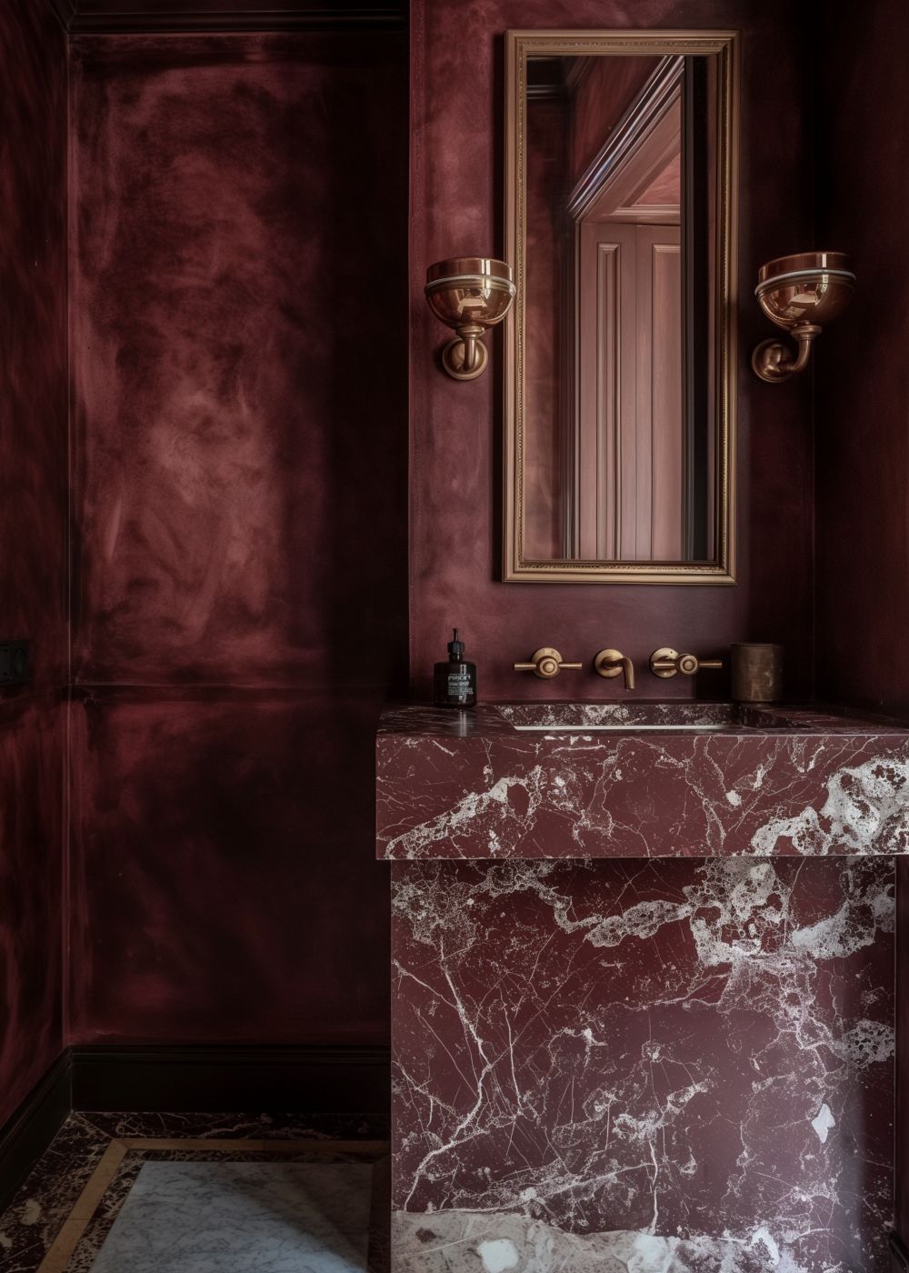 A luxurious moody bathroom featuring deep red textured walls, a red marble vanity with bold white veining, brass wall sconces, and a framed rectangular mirror.