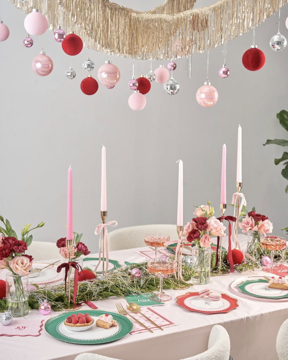 Elegant Christmas tablescape decorated with pink and red candles, festive garland, pastel ornaments, and gold accents for a modern pink holiday look.
