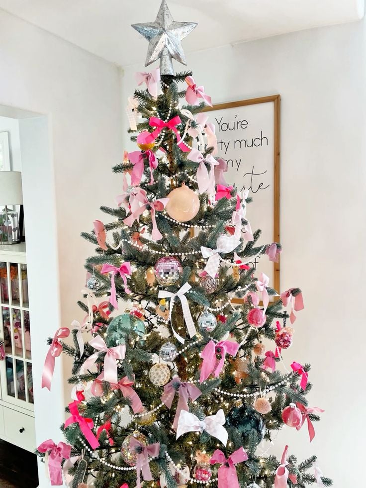 Colorful and playful pink Christmas living room with stockings, oversized bows, a bubblegum Santa art print, and a festive holiday display.