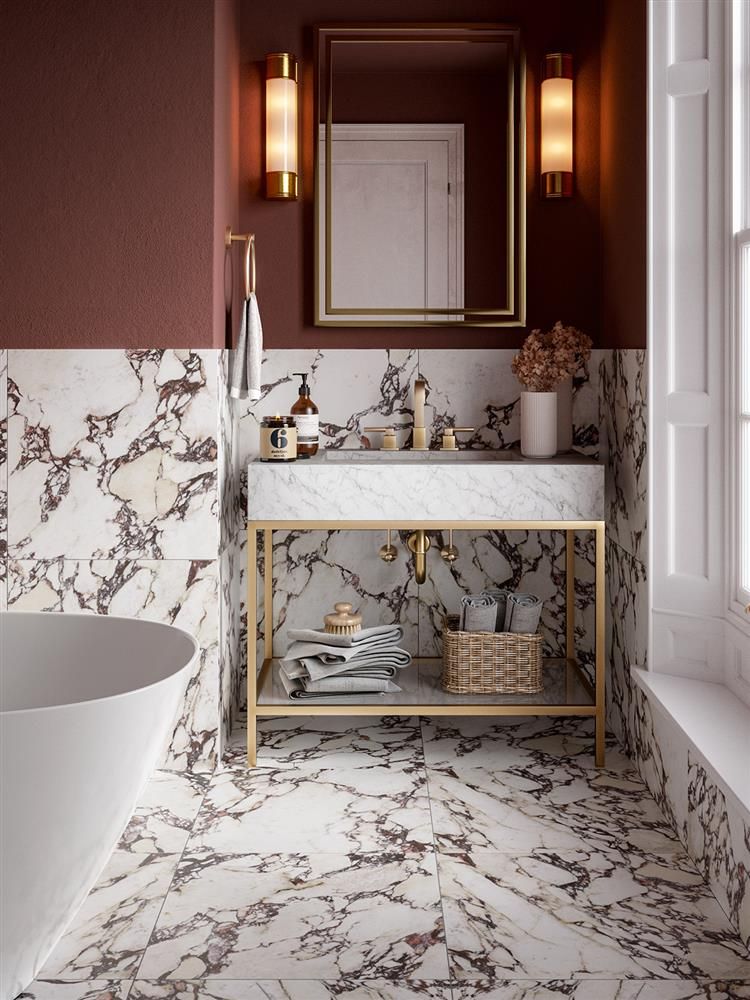 A sophisticated bathroom featuring red and white marble flooring and wall tile, a brass-framed marble vanity, warm red painted walls, and modern brass sconces.
