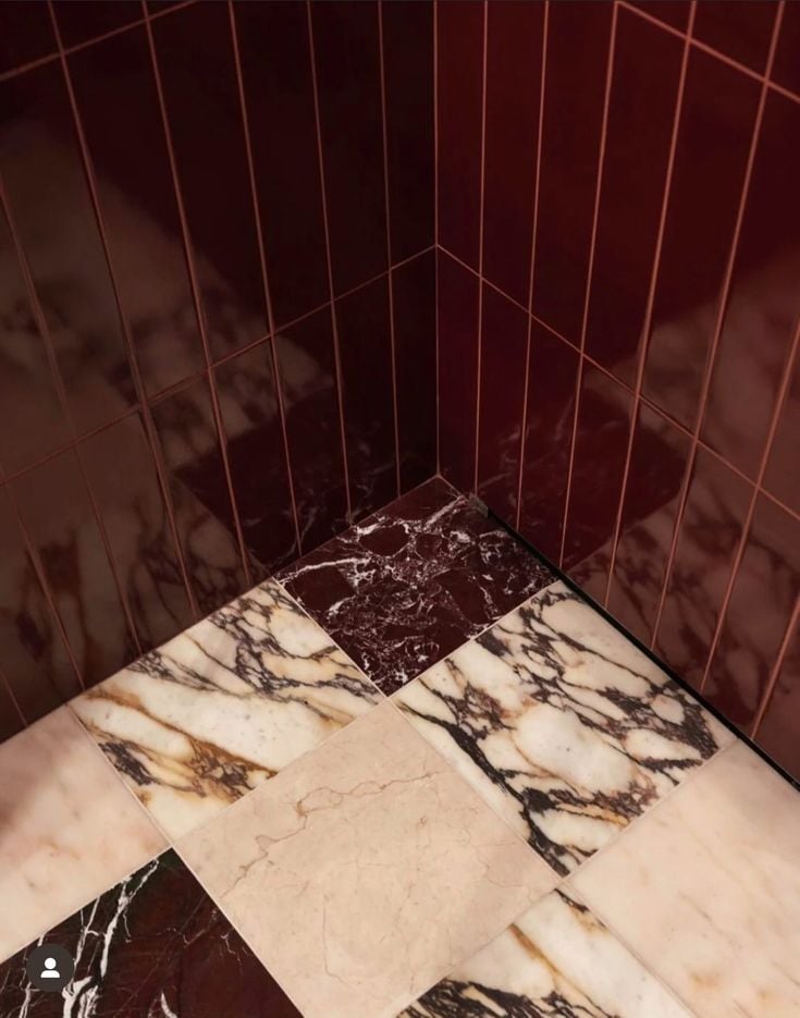 A bathroom corner featuring glossy deep red vertical wall tiles paired with a checkerboard floor made of mixed red, beige, and white marble slabs with bold veining.