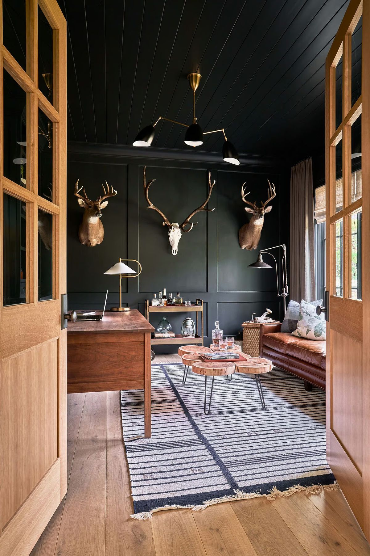 Moody minimal deer aesthetic room featuring dark paneled walls, mounted deer accents, and warm wood furniture