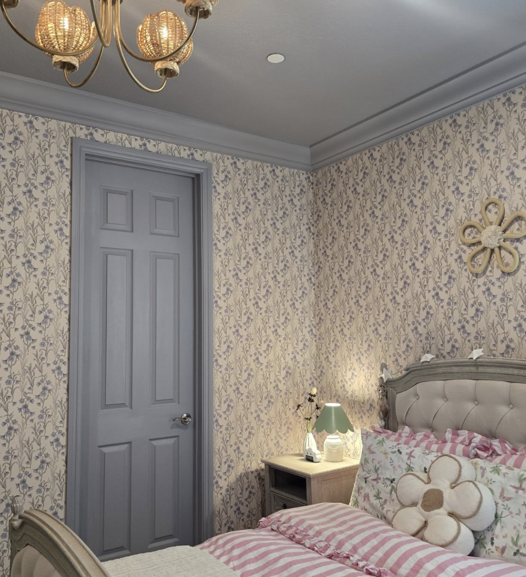 Girls bedroom with soft blue floral wallpaper, gray door, vintage-style bed, and pink striped bedding