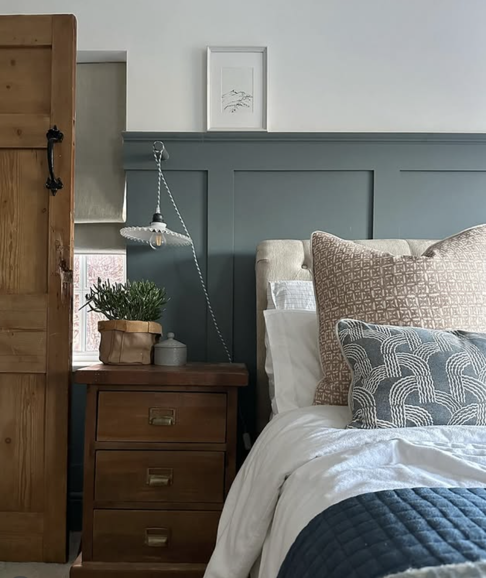 Bedroom with deep blue wainscoting, upholstered beige headboard, layered neutral and blue pillows, and warm wood nightstand