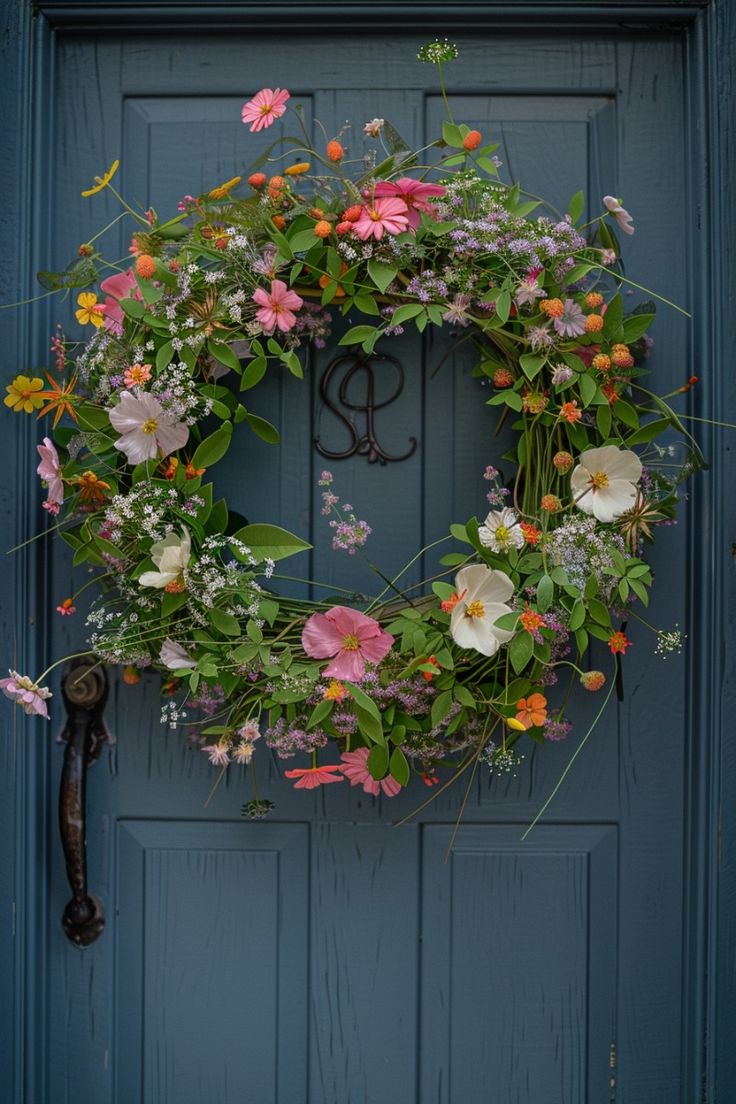 Cottage-style spring wreath with pink, white, and orange wildflowers and natural greenery hanging on a deep blue front door