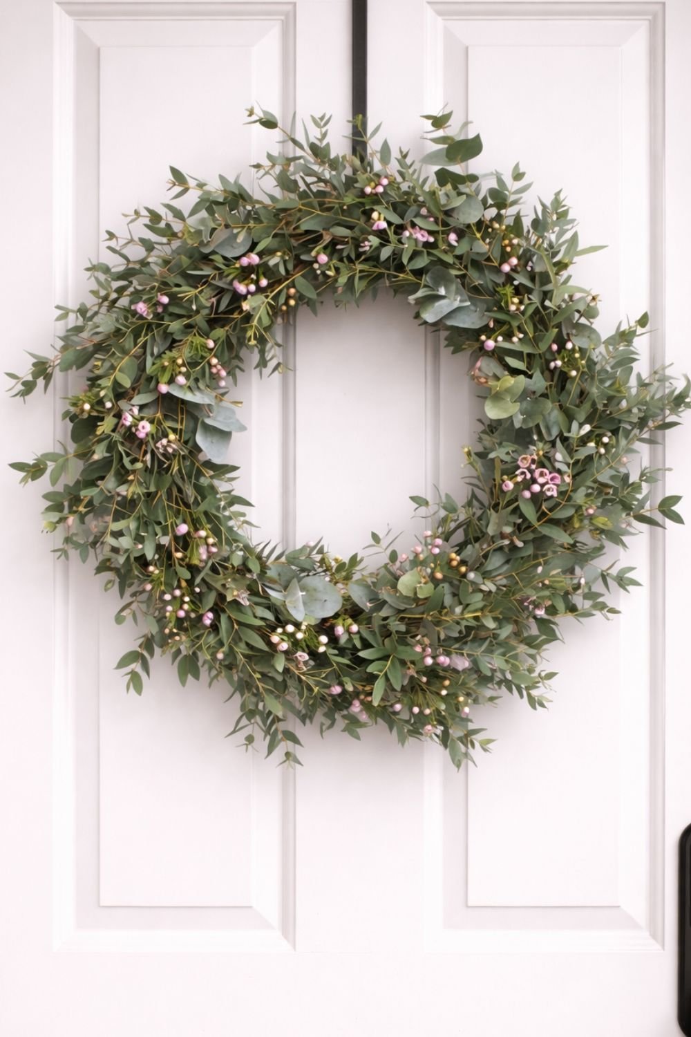 Green eucalyptus spring wreath with soft pink berry accents hanging on a white paneled front door