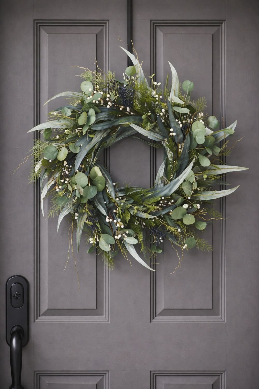 Modern greenery spring wreath with eucalyptus leaves, soft foliage, and natural texture hanging on a front door