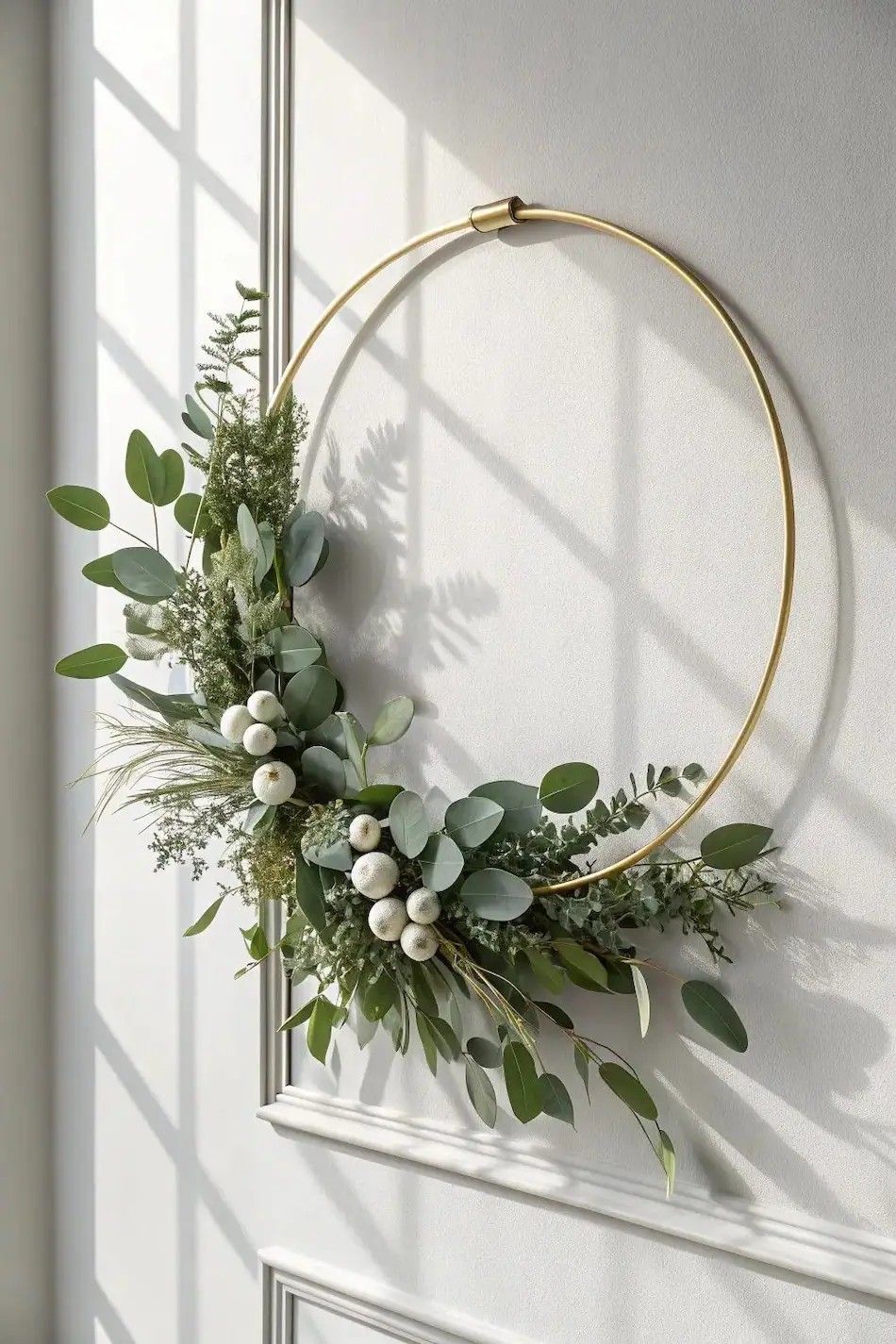 Modern gold hoop wreath with eucalyptus greenery and white berries on a light neutral wall