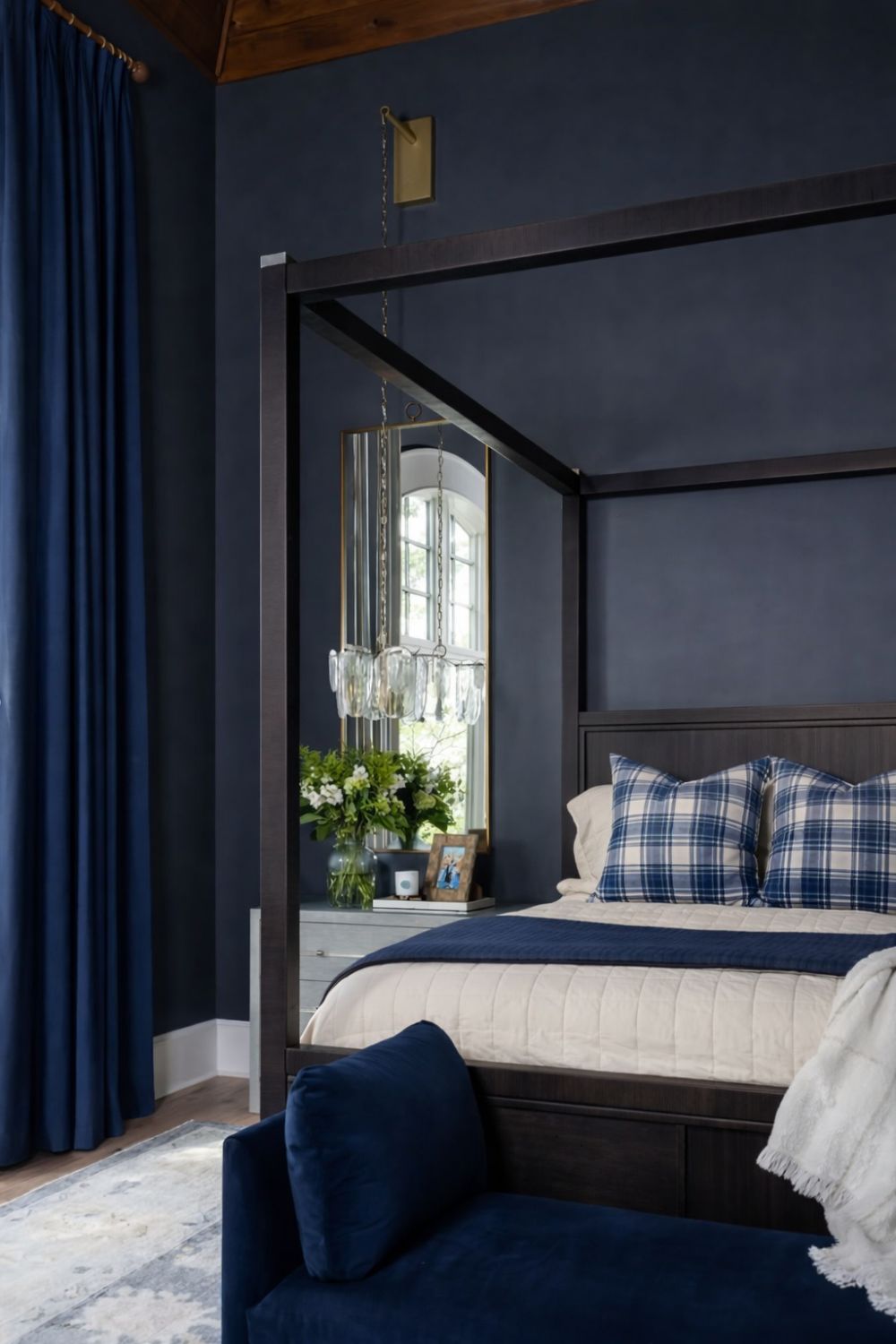 Navy blue bedroom with dark wood canopy bed, plaid pillows, navy bench, and matching navy curtains