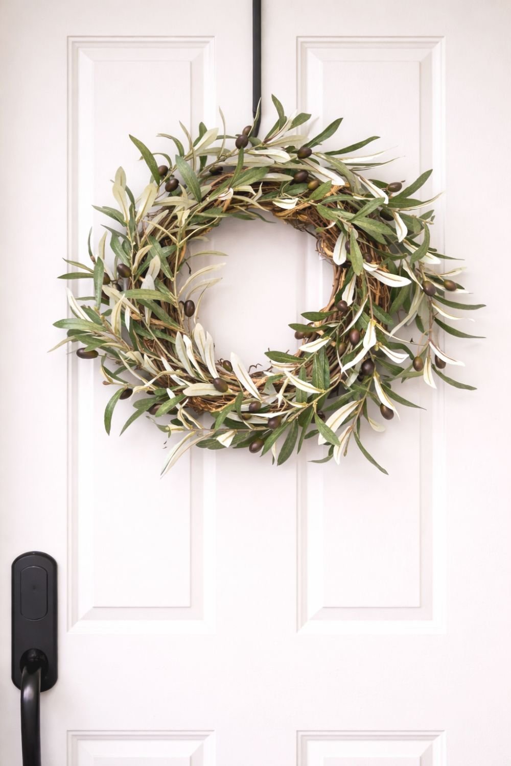 Olive branch wreath with green and silvery leaves and dark olives hanging on a white front door