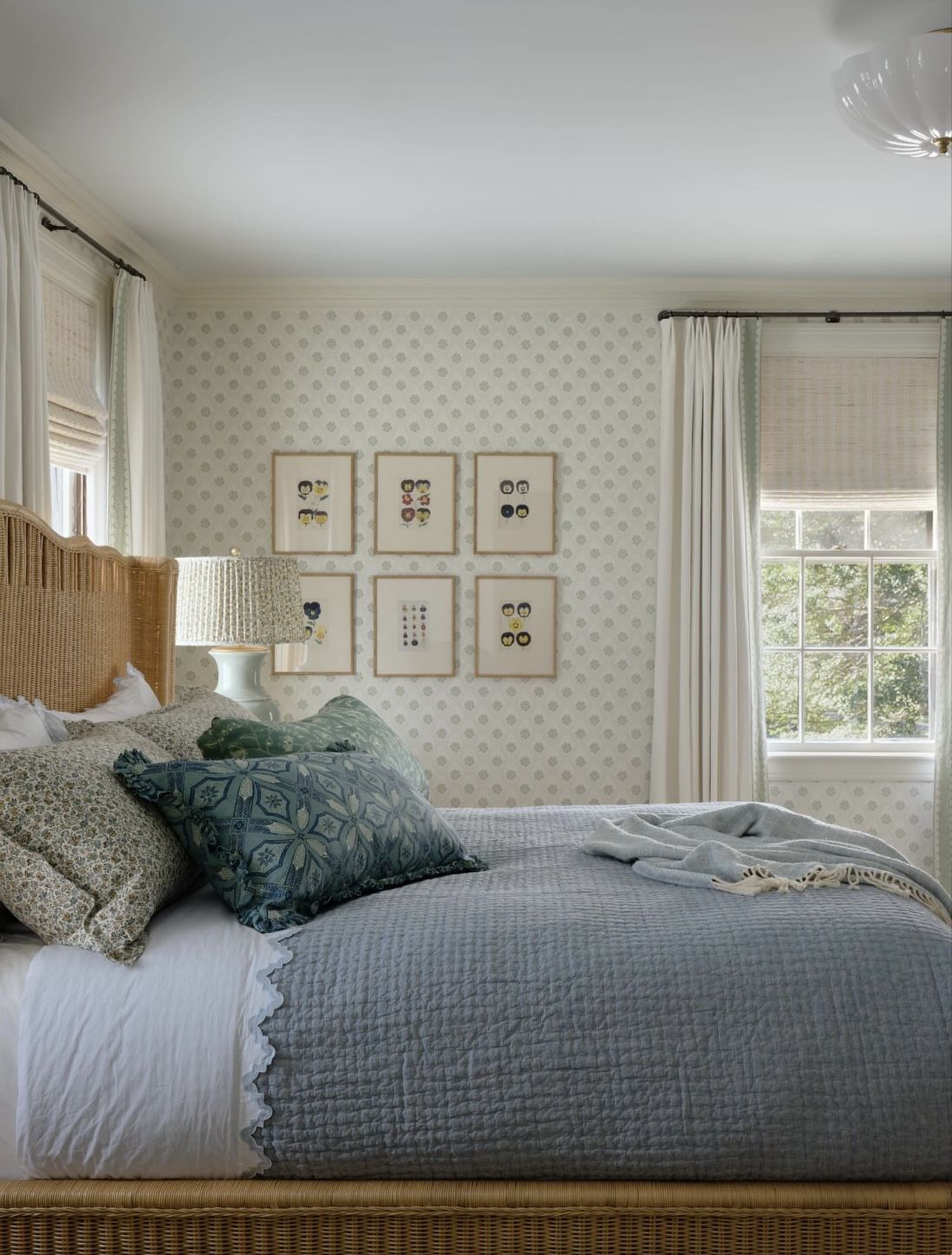 Bright coastal bedroom with woven rattan bed, soft blue quilt, patterned wallpaper, and white curtains by sunlit windows