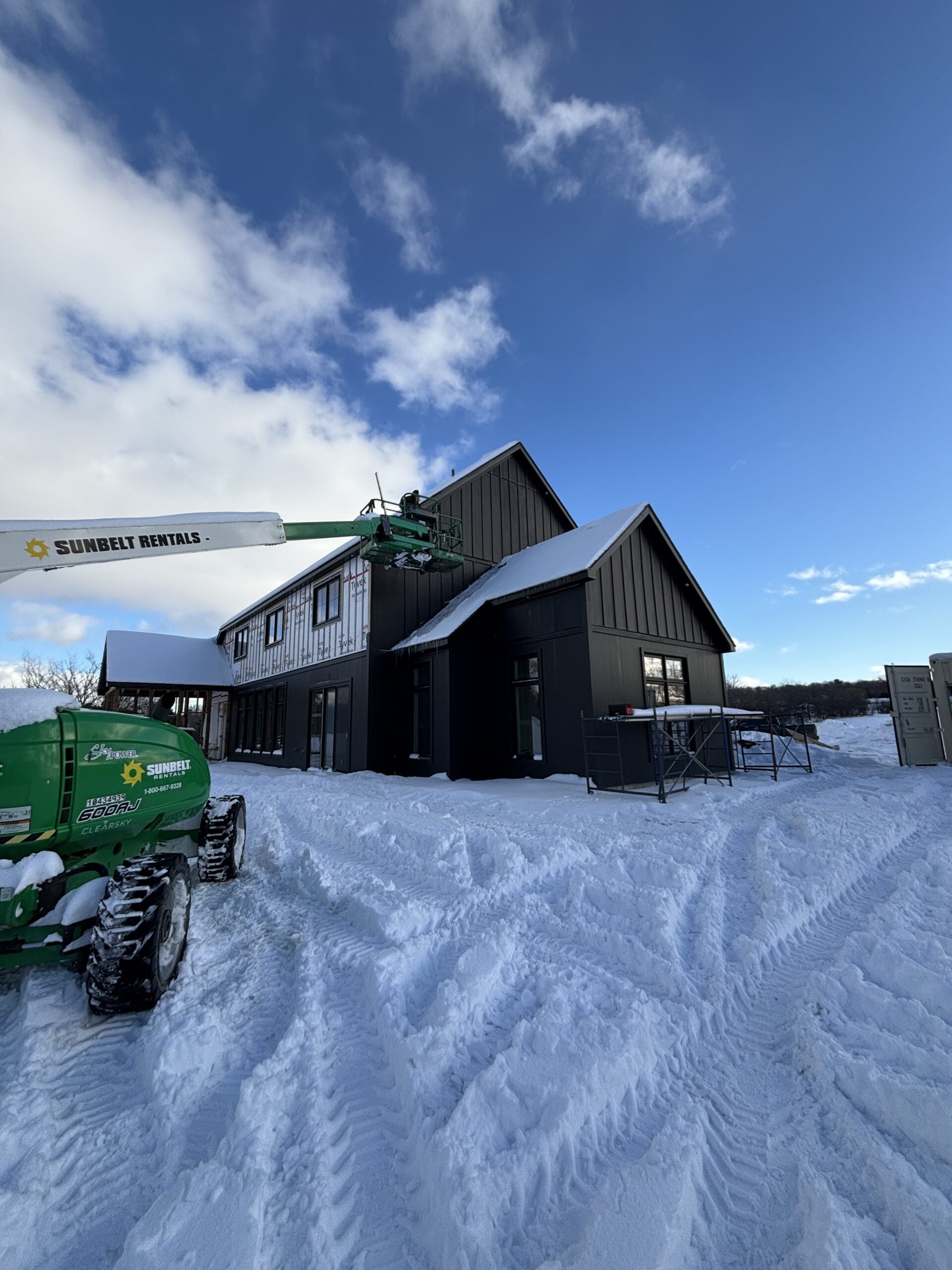 Black board and batten siding on our modern farmhouse exterior during winter construction, showing the contrast of black siding against snow on our rural Ontario property.