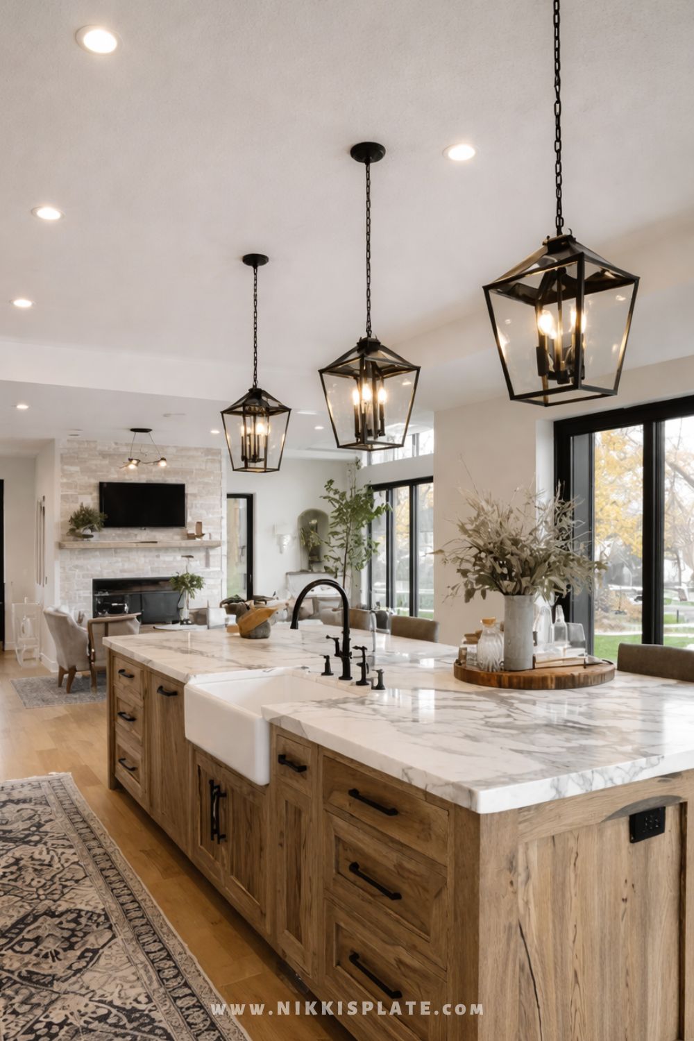 Modern farmhouse kitchen with black lantern pendant lights hanging above a large wood island with a white farmhouse sink and marble countertop.
