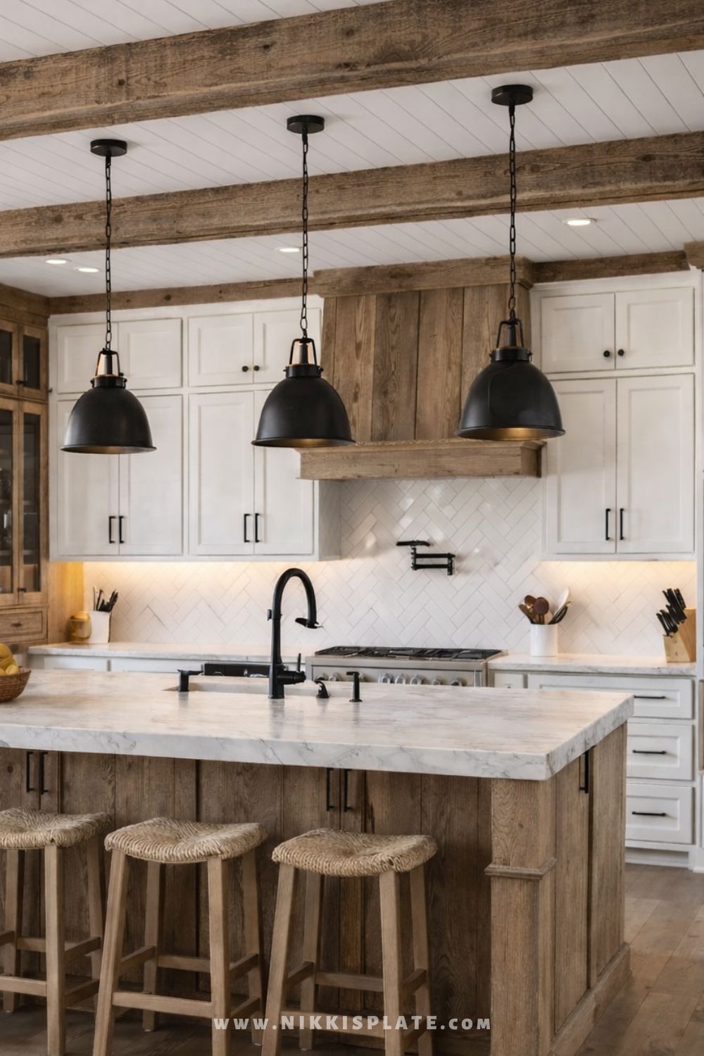 Rustic farmhouse kitchen with black pendant lights hanging over a wood kitchen island with woven stools, white cabinetry, and exposed wood beams.