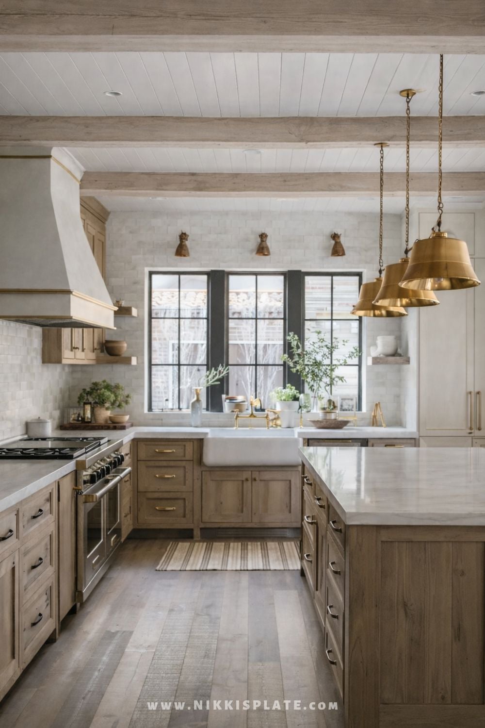 Rustic farmhouse kitchen with brass pendant lights over a large island, light wood cabinetry, white farmhouse sink, and exposed wood ceiling beams.