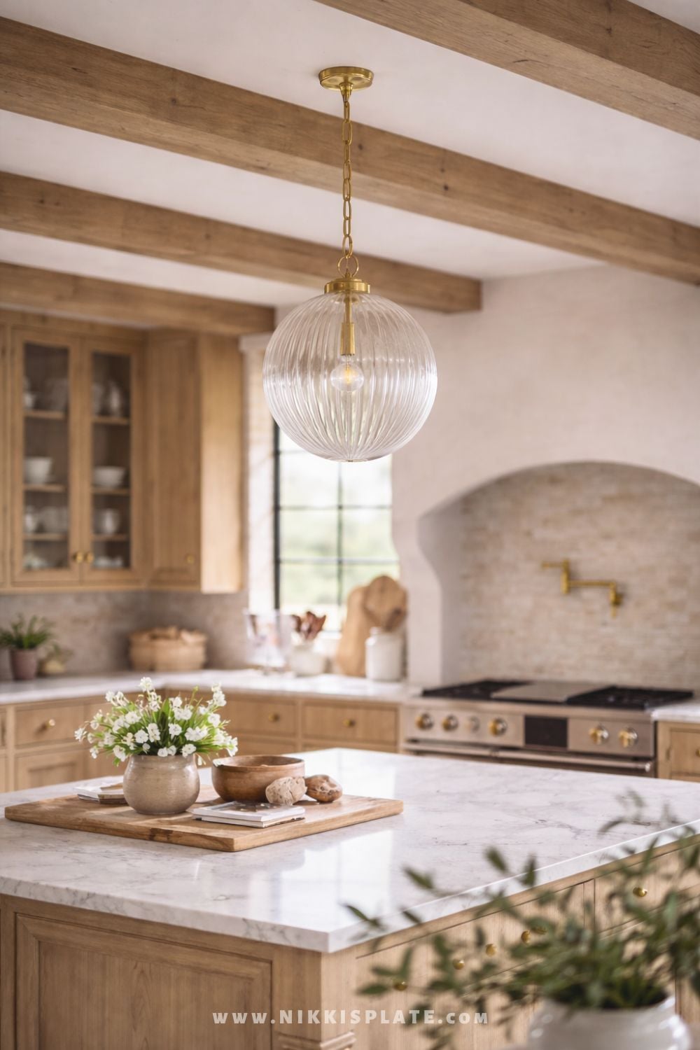 Ribbed glass globe pendant light with brass hardware hanging above a marble kitchen island in a warm farmhouse kitchen.
