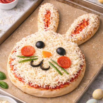 Healthy Sourdough Easter Bunny Pizza on a baking sheet at an angle, topped with mozzarella, olives, pepperoni, and bell peppers for a festive Easter dinner idea.