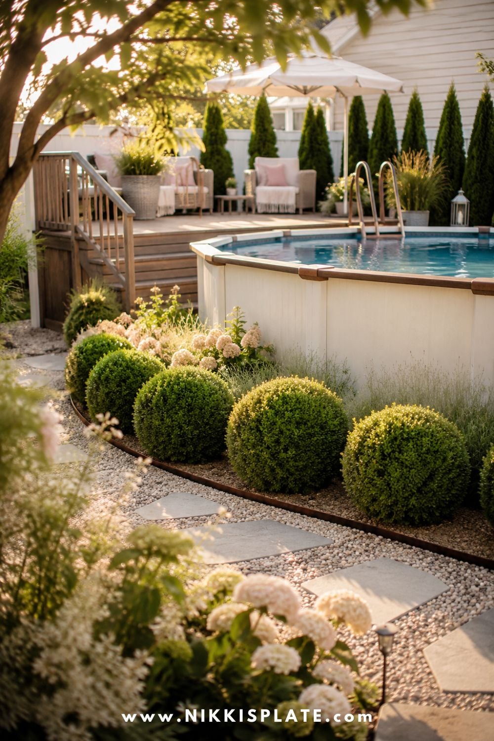 Tall above ground pool with round boxwoods, soft hydrangeas, gravel walkway, warm wood deck, and clean backyard landscaping.